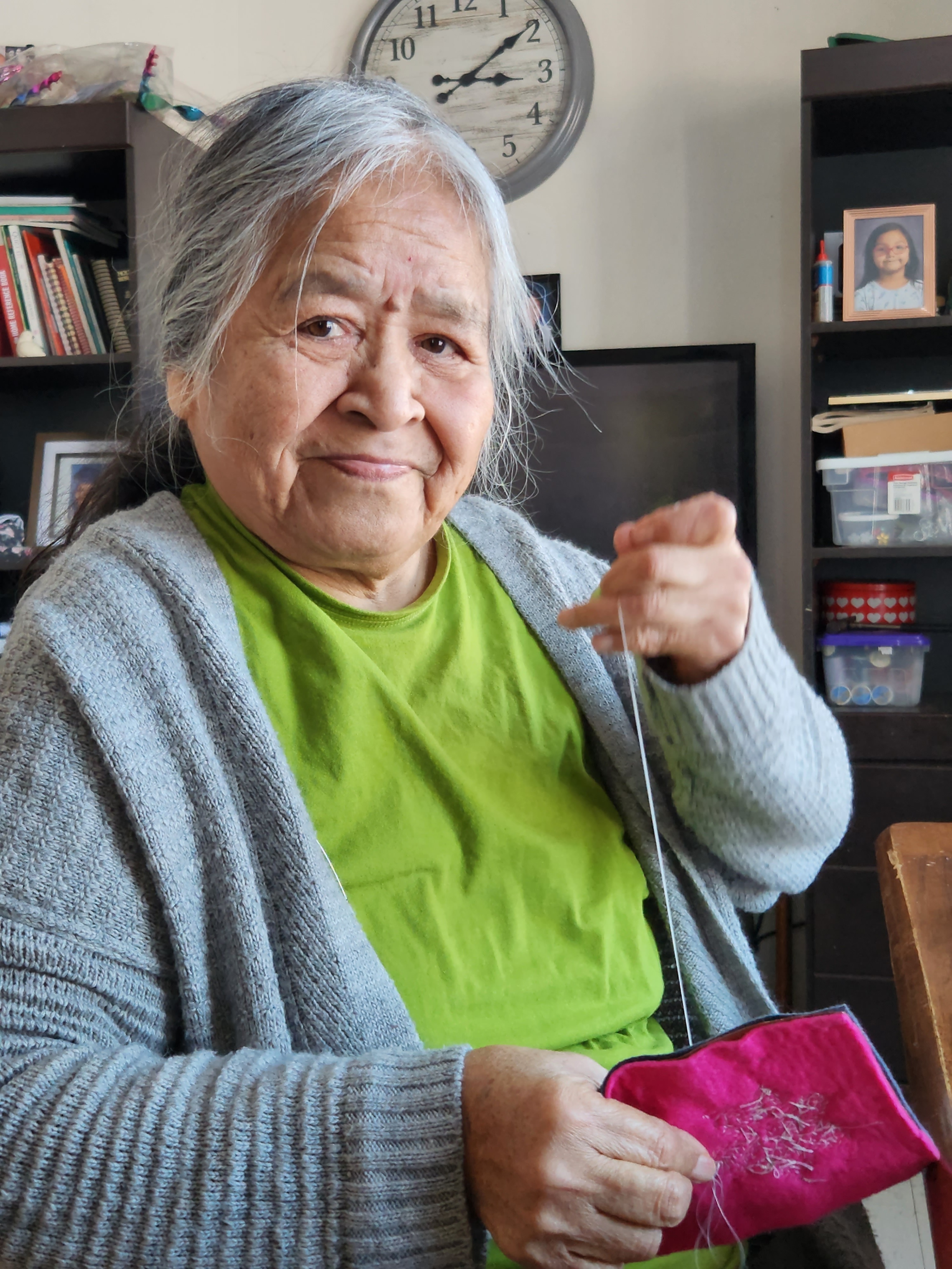 A woman smiling, holding a pink bag sewing beading