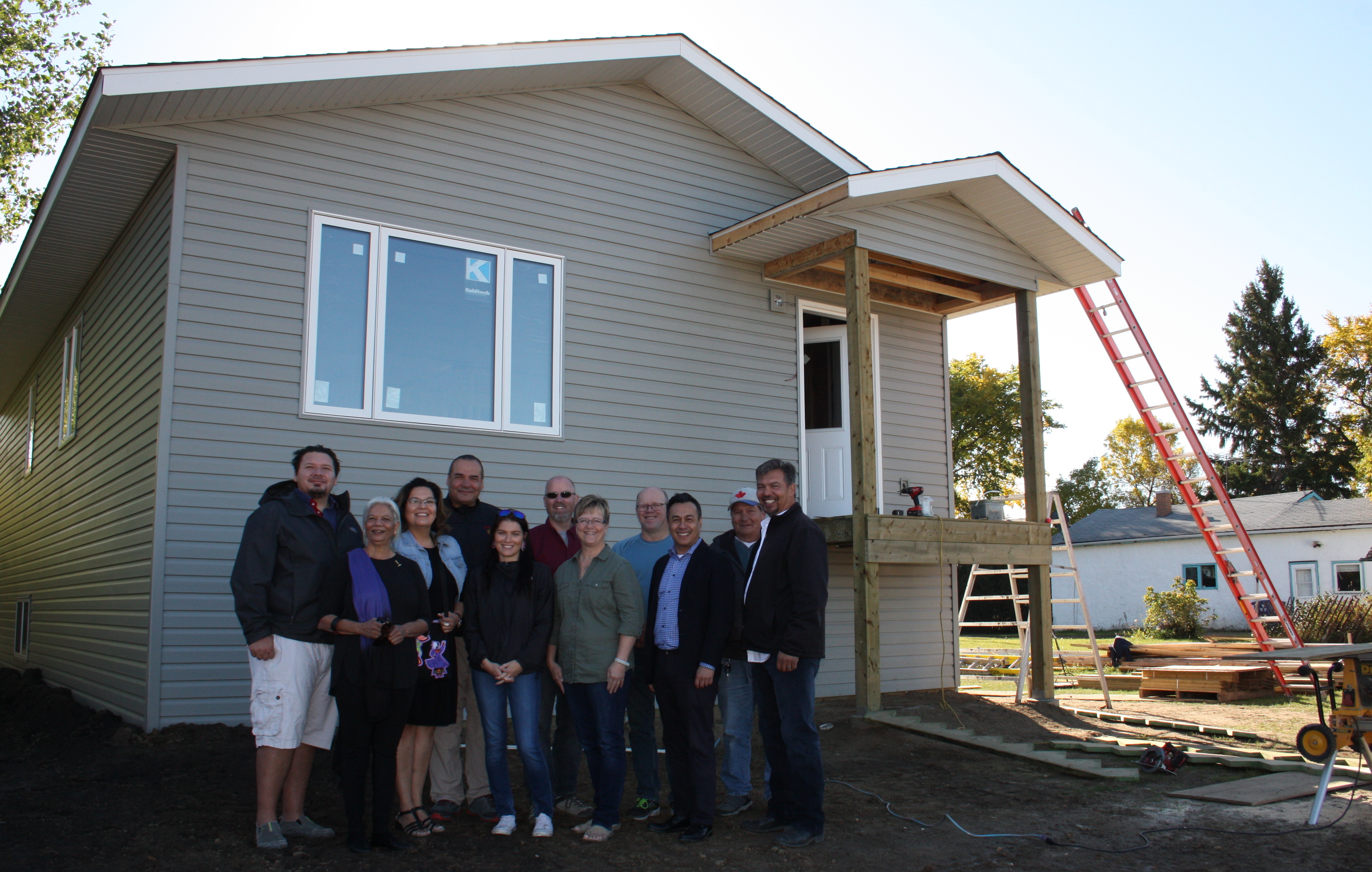 Group of 11 people standing in front of the first new home built in Duck Lake