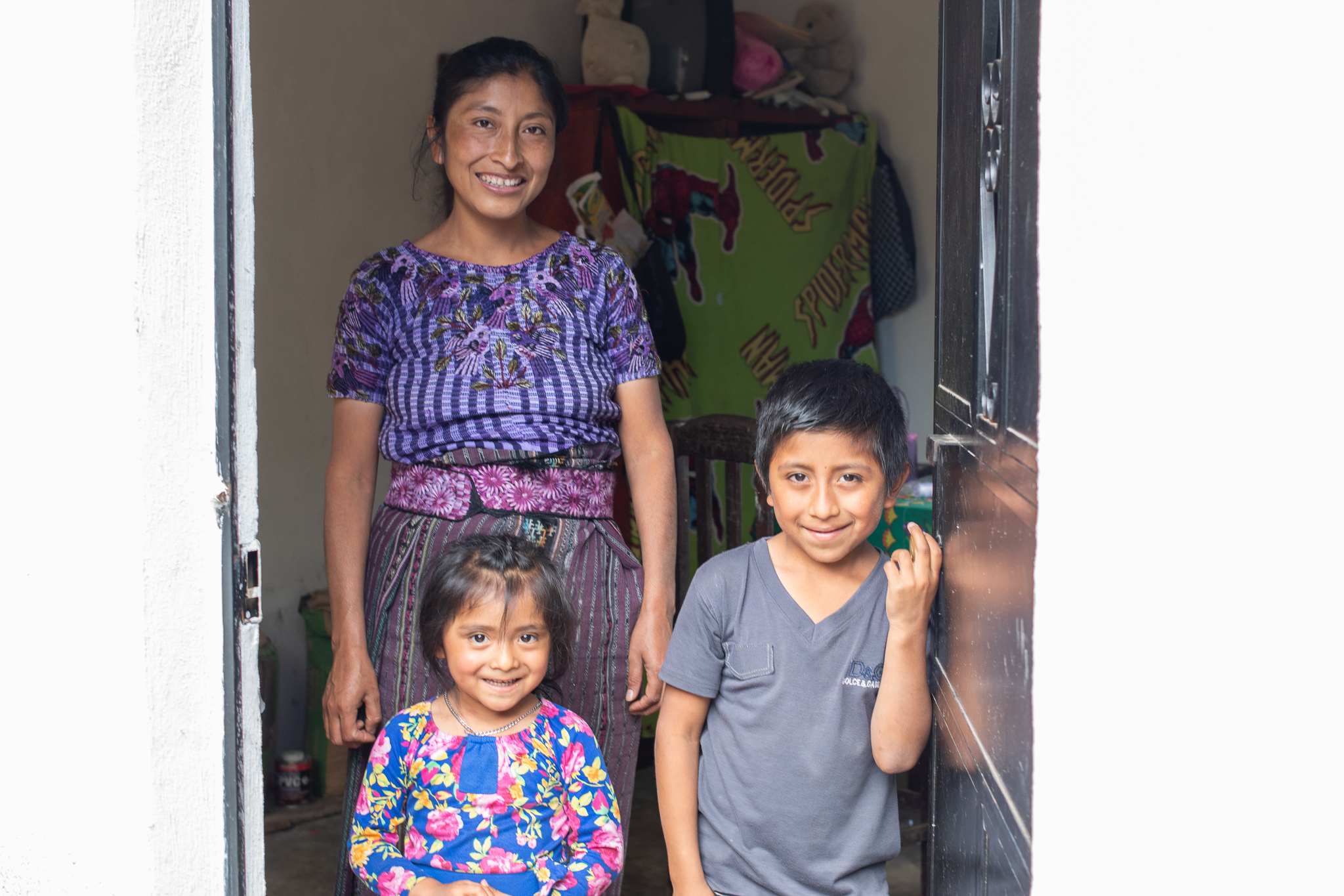 Maria standing with 2 of her kids at the doorway all with big smiles in Guatemala