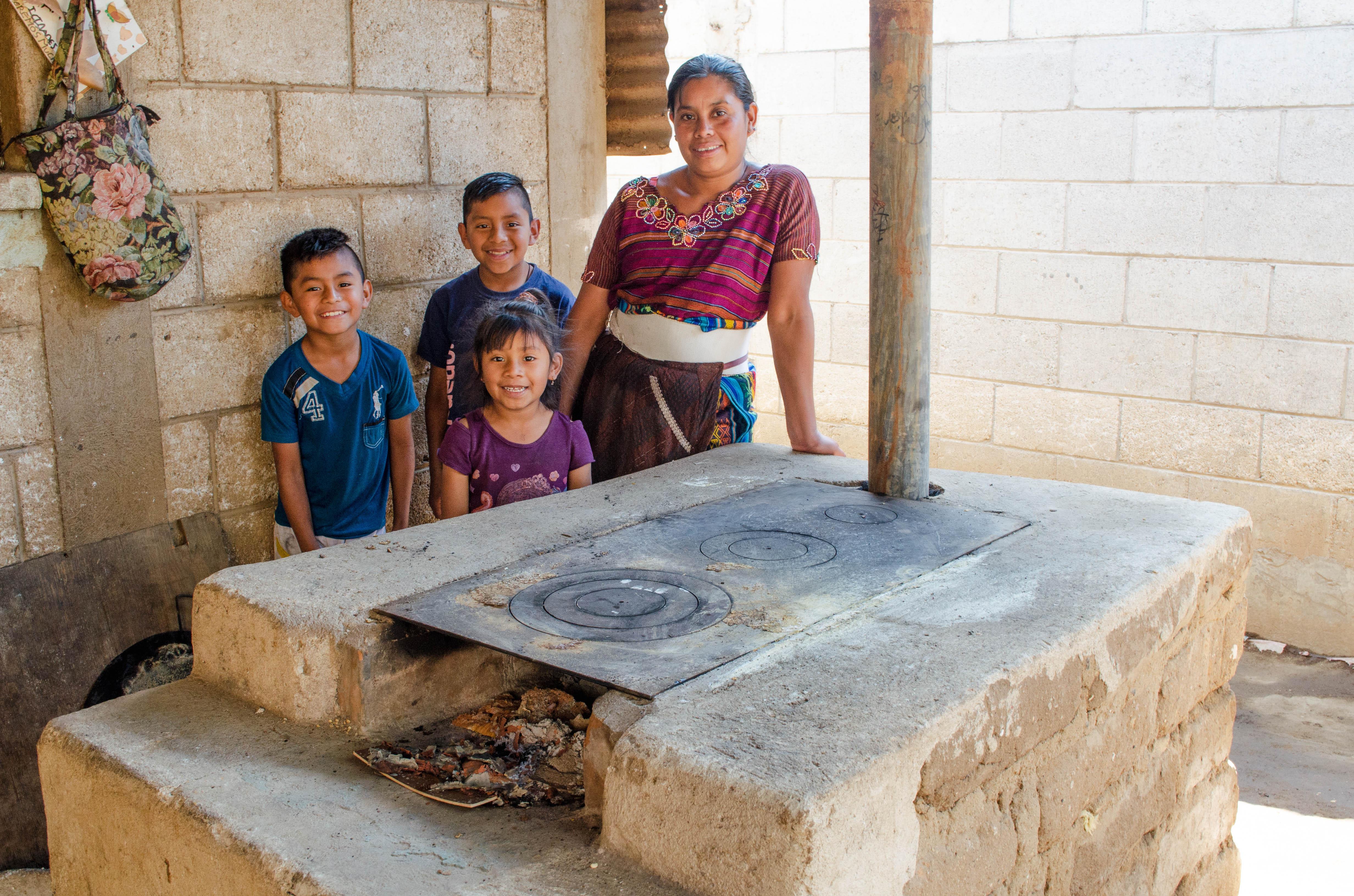 A woman and her 3 young children stand smiling with their new smokeless stove