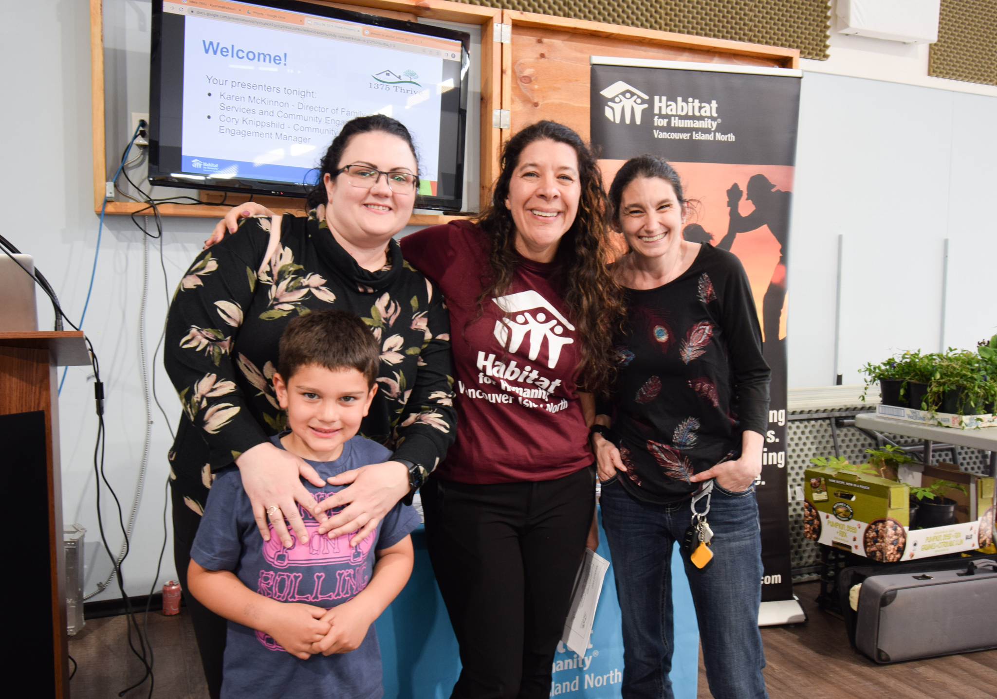 Habitat's Family Resources Manager is pictures with two future homeowners standing in front of the future built presentation screen.