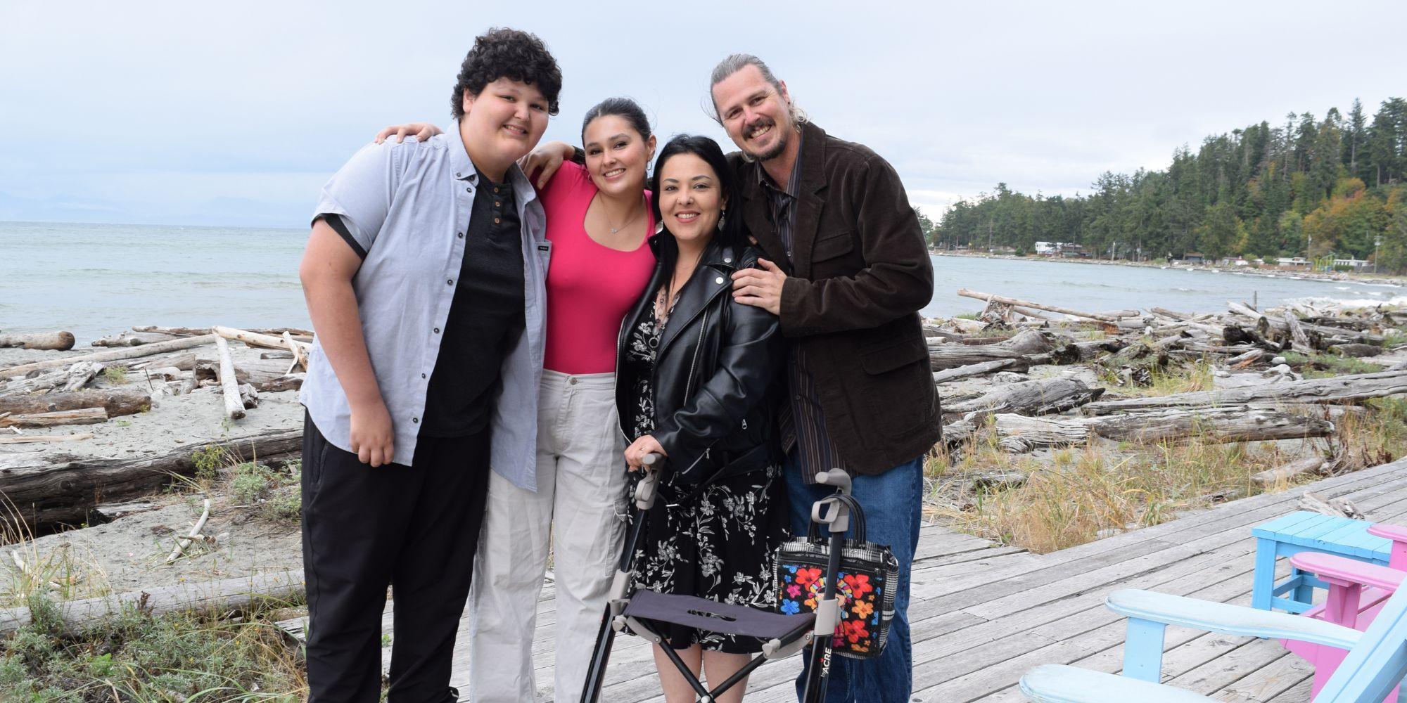Eric, Michelle and their two children embracing on a Vancouver Island beach. Michelle is holding a walker.